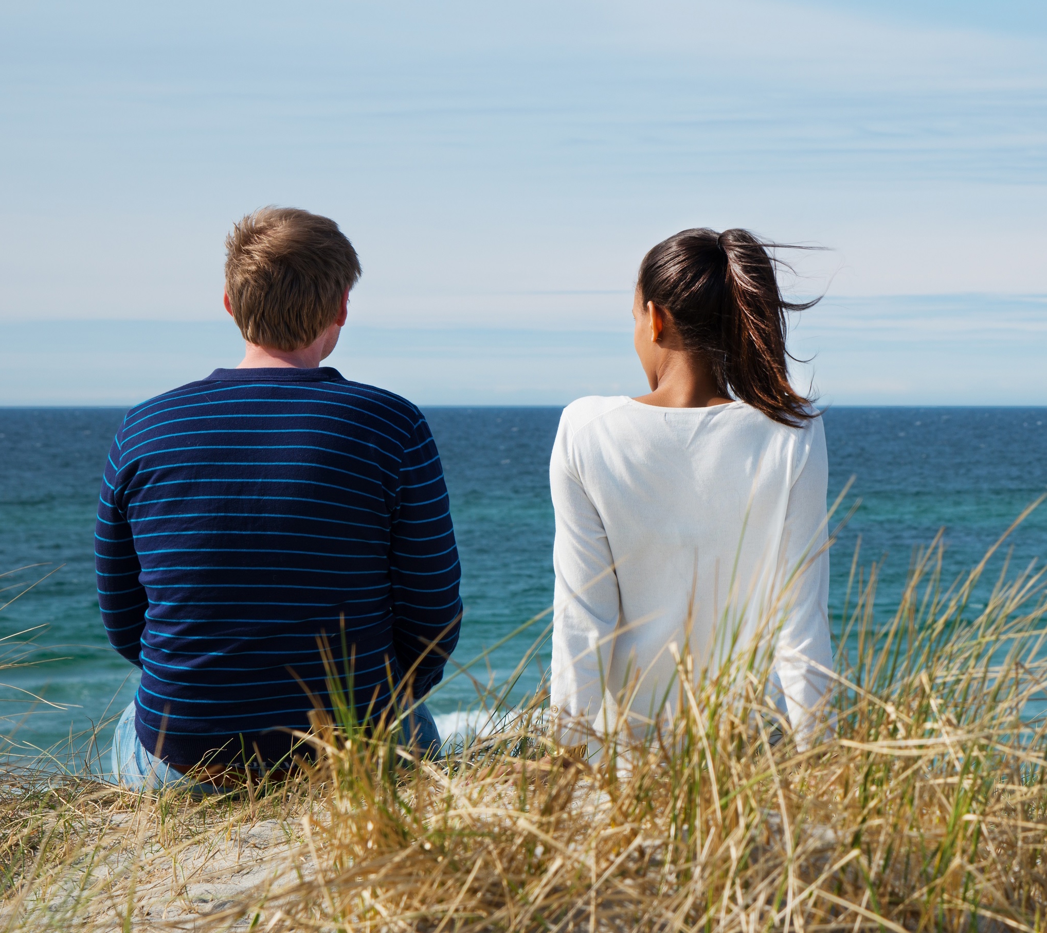 En mann og kvinne som sitter i høyt gress og ser på havet